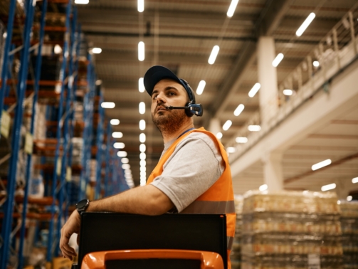 Warehouse worker driving forklift while working at storage compartment.